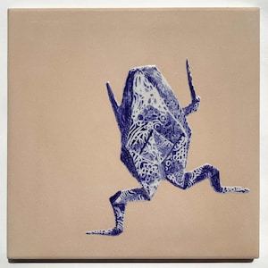 May include: A square ceramic tile featuring a blue origami frog design. The frog is depicted in a running pose with intricate patterns, set against a beige background. The artwork has a handcrafted aesthetic.