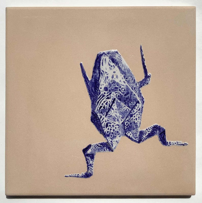 May include: A square ceramic tile featuring a blue origami frog design. The frog is depicted in a running pose with intricate patterns, set against a beige background. The artwork has a handcrafted aesthetic.