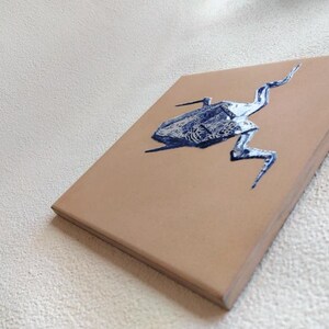 May include: A tan canvas with a blue and silver insect illustration. The artwork is a side view, showcasing the insect's detailed form. The canvas is rectangular and appears to be mounted on a wooden frame.