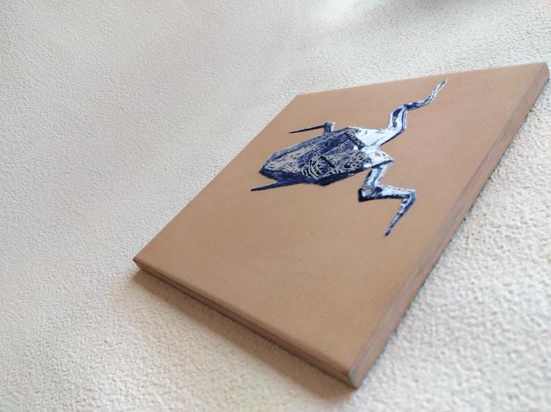 May include: A tan canvas with a blue and silver insect illustration. The artwork is a side view, showcasing the insect's detailed form. The canvas is rectangular and appears to be mounted on a wooden frame.