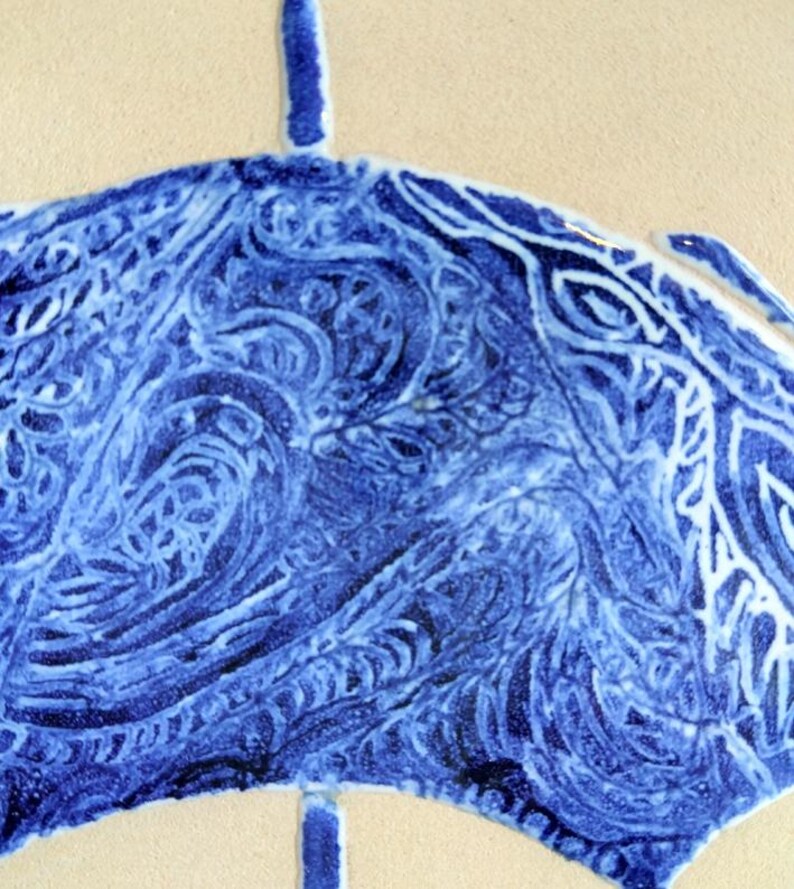 Może przedstawiać: Zbliżenie niebiesko-białej płytki ceramicznej z motywem stylizowanego parasola. Parasol ma szczeg&oacute;łowy, wirujący wz&oacute;r w odcieniach niebieskiego na kremowym tle. Projekt przypomina tradycyjną ceramikę.
