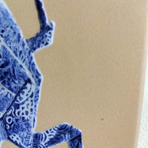 May include: Close-up of a ceramic tile with a blue and white decorative design. The design features a stylized, abstract shape with intricate patterns. The tile has a beige background.