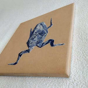 May include: A square canvas art piece featuring a blue and white origami frog design. The frog is depicted in a running pose against a tan background. The artwork has a modern, minimalist aesthetic.