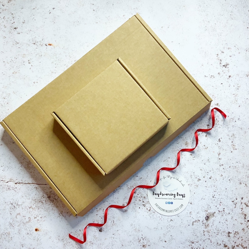 May include: Two brown cardboard boxes, one nested inside the other, with a red ribbon and a round sticker that says "Daydreaming Days".