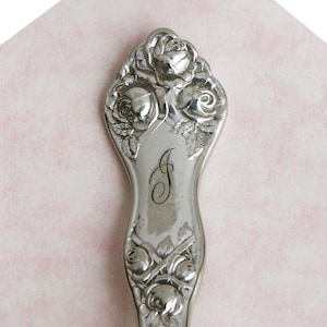 May include: Silver spoon with a rose design and the letter "J" engraved on the handle.