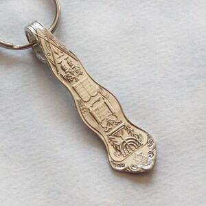 May include: Silver-toned keychain shaped like a spoon with a detailed design featuring a menorah, a Star of David, and Hebrew text.