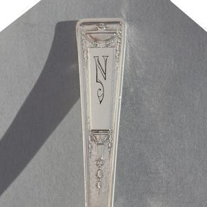 May include: Silverware handle with an ornate design and the letter "N" engraved on the front.