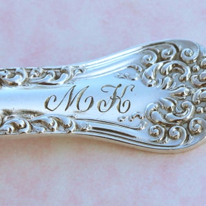 May include: Silverware with an ornate design and the initials "M K" engraved on the handle.