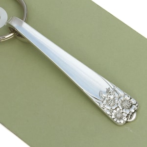 May include: Silver key chain with a floral design. The design features a cluster of stylized flowers with a raised, textured surface.