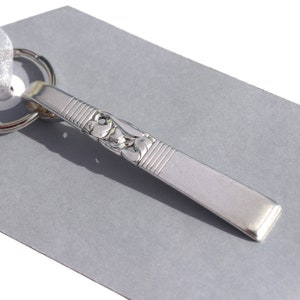 May include: A silver key chain with a decorative design. The key chain is made from a repurposed spoon.