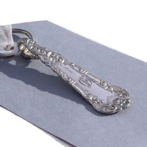 May include: Silver spoon keychain with an ornate design and a letter "C" engraved on the handle.