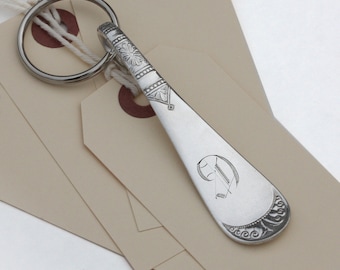 May include: A silver key chain with a decorative handle and a key ring. The handle is engraved with a floral design and the letter "D".