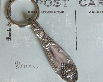 May include: A silver spoon keychain with a grapevine design. The spoon is attached to a silver key ring.