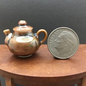 May include: A small, brown and blue ceramic teapot with a shiny glaze. The teapot is about the size of a US dime.