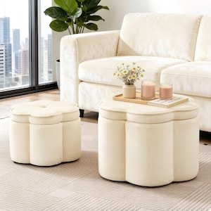 May include: Cream-colored, clover-shaped ottoman and matching coffee table set. The ottoman has a cushioned top and rounded sides. The coffee table features a tray with candles and a vase of flowers. A cream-colored sofa is in the background.
