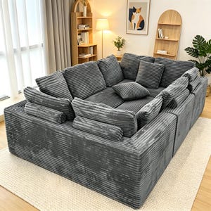 May include: A large, modular gray corduroy sectional sofa with multiple cushions and pillows. The sofa is arranged in a square shape and sits on a cream-colored rug. The corduroy fabric has a ribbed texture.