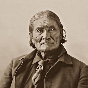 May include: A black and white portrait of an older man with long gray hair. He is wearing a dark jacket with a tie and a button-up shirt. The photo is faded and has a vintage look.