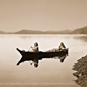 May include: Two people in a canoe paddling on a calm lake with mountains in the background.