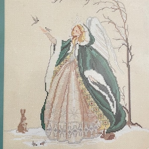 May include: A counted cross stitch kit titled "Snow Angel" by Mar Bek. The design features an angel in a green and cream gown, with a rabbit and bird. The framed size is 12 x 15 inches.