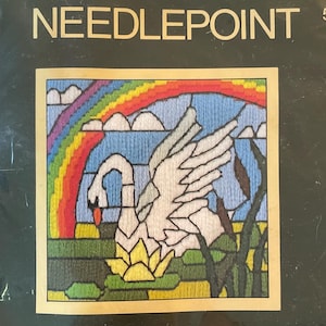 May include: A Sunset Needlepoint kit featuring a stained glass swan design. The kit includes a printed design on 6.5" x 6.5" canvas, wool yarn, needle, and instructions. The finished design fits a 5" x 5" frame. The image shows a swan under a rainbow.