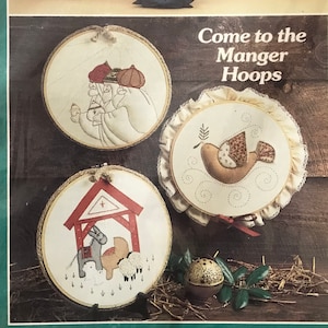 May include: A set of three embroidery hoop patterns for a Christmas manger scene. The patterns include a dove, a manger with animals, and three wise men. The patterns are designed for 10-inch hoops. "Come to the Manger Hoops" is printed on the front of the package.
