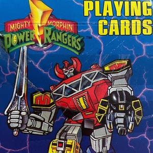 May include: A deck of "Mighty Morphin Power Rangers" playing cards. The box is blue with the words "PLAYING CARDS" in yellow. The front features a red, yellow, and black robot holding a sword, with a lightning bolt background.