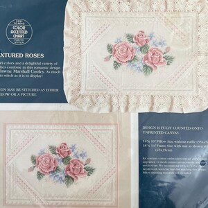 May include: Sunset needlepoint kit featuring a floral design with pink roses and blue accents. The kit includes unprinted canvas, embroidery thread, and instructions. The finished pillow size is 14" x 10" (35x25cm).