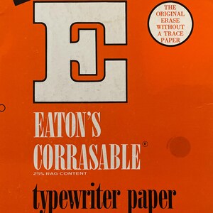 Może przedstawiać: Pomarańczowe pudełko papieru do pisania na maszynie Eaton's Corrasable. Pudełko zawiera duże białe logo "E" oraz tekst "80 arkuszy" i "Średnia waga". Dodatkowy tekst to "Perforowane do standardowego segregatora 3-pierścieniowego" i "Oryginalne wymazywanie bez śladu".