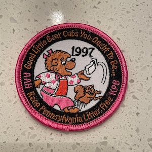 May include: A pink and black embroidered patch with a cartoon bear holding a trash bag. The text on the patch reads "Good Little Bear Cubs You Ought To Be... RAH Keep Pennsylvania Litter Free KPB" and "1997".