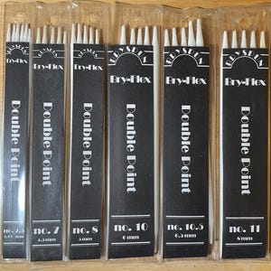 May include: Six packages of Bry-Flex double-point knitting needles in various sizes. Each package is black with white text, including the needle size in millimeters. The needles are white and visible through the clear packaging.