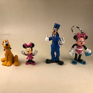May include: Four Disney character figurines: Pluto the dog, Minnie Mouse in a pink dress, Goofy in a blue suit, and Minnie Mouse in a red and white swimsuit.