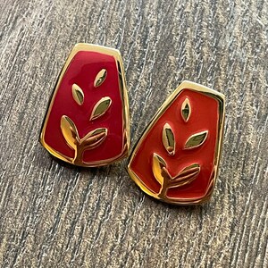 May include: A pair of red and gold earrings with a leaf design. The earrings are shaped like a teardrop and have a gold border.