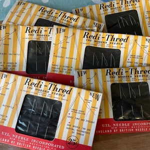 May include: A close-up of several vintage packaging boxes for Redi-Thred needles. The boxes are yellow and red with black and white illustrations of the needles. The text on the boxes reads "Redi-Thred The Modern Needle".