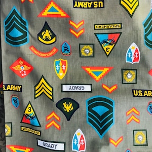 May include: A green fabric with a repeating pattern of military insignia, including the words "U.S. Army", "Spearhead", and "Grady". The insignia are in various colors, including red, blue, yellow, and white.