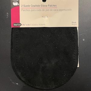 May include: Two black suede cowhide elbow patches, 4 3/4 inches by 6 inches, for repairing or reinforcing clothing. The patches are packaged on a white card with the text "2 Suede Cowhide Elbow Patches" and "Parches para codo de piel de vaca agamuzado".
