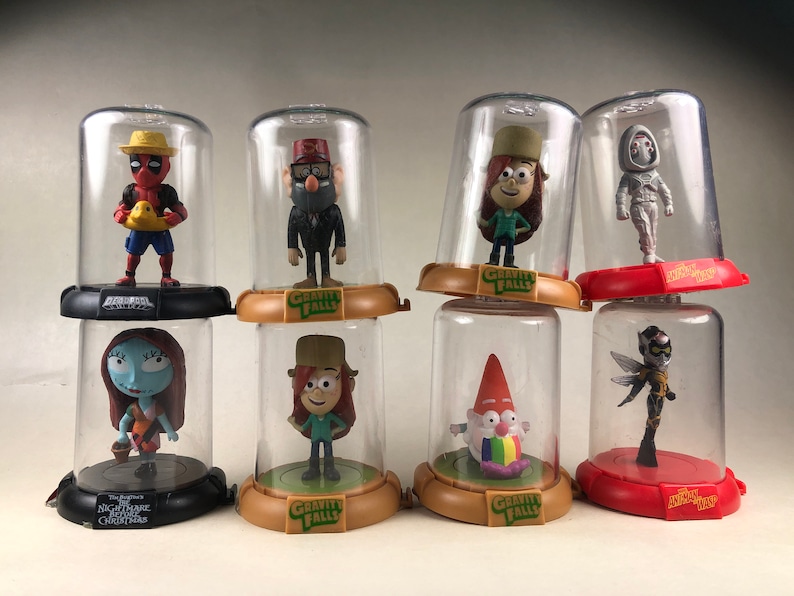 Puede incluir: Ocho figuras de personajes diferentes se muestran en c&uacute;pulas de pl&aacute;stico transparente. Los personajes incluyen Deadpool, Stan Pines, Mabel Pines, Bill Cipher, Dipper Pines, un gnomo, Sally y una abeja. Cada c&uacute;pula tiene una base con el nombre del programa del personaje impreso en ella.