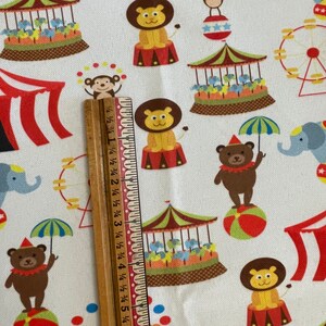 May include: White fabric with a colourful circus pattern. The pattern includes a lion, a monkey, a bear, an elephant, a Ferris wheel, a carousel, and a tent. The fabric is perfect for quilting, sewing, and crafting.