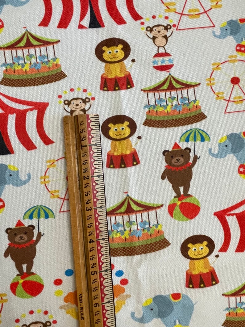 May include: White fabric with a colourful circus pattern. The pattern includes a lion, a monkey, a bear, an elephant, a Ferris wheel, a carousel, and a tent. The fabric is perfect for quilting, sewing, and crafting.