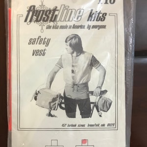 May include: A black and white photo of a person wearing a safety vest and riding a bicycle. The vest is white with a red 'R' on the front. The photo is from a vintage Frostline Kits catalog. The text on the page reads 'Frostline Kits, the kits made in America, by everyone. Safety vest. 452 Burbank Street Broomfield, Colo. 80020. Medium. X-Large.'