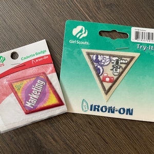 May include: Two Girl Scout badges, one for "Marketing" and one for "Try-Its". Both badges are iron-on and feature a colorful design.