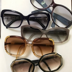 May include: A collection of four pairs of eyeglasses with different frame styles and colors. The frames are made of plastic and metal. The lenses are tinted.