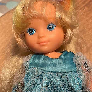 May include: A vintage doll with long blonde hair and blue eyes, wearing a blue and white dress with a sparkly tulle overlay.