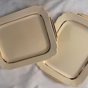 May include: Two white serving trays with gold trim. The trays are rectangular and have a slightly raised edge.