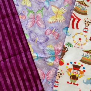 May include: Three fabric swatches, one with a purple and white striped pattern, one with a purple background and a repeating pattern of colourful butterflies, and one with a white background and a repeating pattern of circus-themed illustrations including a clown, an elephant, a Ferris wheel, and a tent.