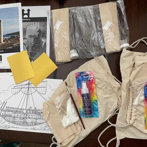 May include: An assortment of craft supplies, including tie-dye kits, paintbrushes, and coloring pages with illustrations of ancient ships and architectural ruins. The image also shows gold-colored paper and printed materials with the word "PHOENICIA".