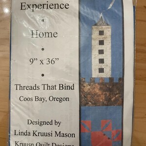 May include: A white paper pattern with a blue and red quilt design. The pattern is for a "Row by Row Experience" quilt titled "Home". The pattern is 9 inches by 36 inches and is designed by Linda Kruusi Mason of Kruusn Quilt Designs.