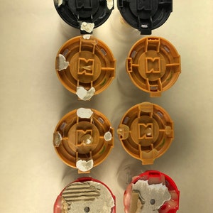 Puede incluir: Seis tapas redondas de pl&aacute;stico con una variedad de colores y dise&ntilde;os. Las tapas est&aacute;n en dos filas de tres. La fila superior tiene dos tapas negras y una tapa dorada. La fila del medio tiene dos tapas doradas y una tapa negra. La fila inferior tiene dos tapas rojas.