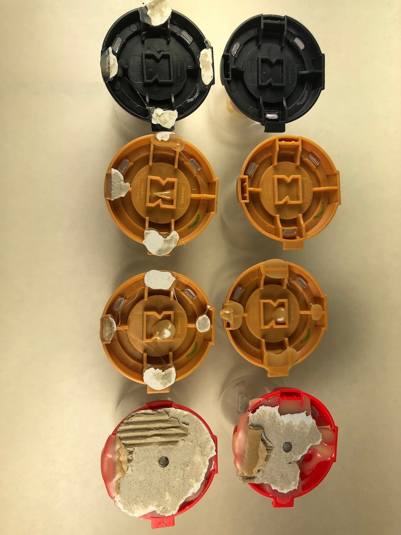 Puede incluir: Seis tapas redondas de pl&aacute;stico con una variedad de colores y dise&ntilde;os. Las tapas est&aacute;n en dos filas de tres. La fila superior tiene dos tapas negras y una tapa dorada. La fila del medio tiene dos tapas doradas y una tapa negra. La fila inferior tiene dos tapas rojas.