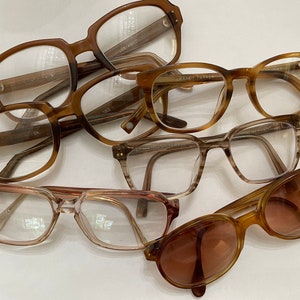 May include: A collection of six pairs of brown eyeglasses with various frame styles and lens shapes. Some of the frames have text on them, including "WHITNEY PARKER" and "1203".