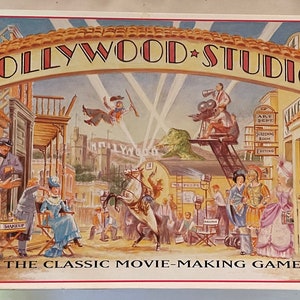 Puede incluir: Una caja de juego de mesa vintage con una ilustración colorida de un set de estudio de cine de Hollywood. La caja tiene el título "HOLLYWOOD STUDIO" en letras rojas y blancas con una estrella entre las palabras. La ilustración representa un set de filmación bullicioso con actores, directores y miembros del equipo. El texto "THE CLASSIC MOVIE-MAKING GAME" está impreso debajo del título.